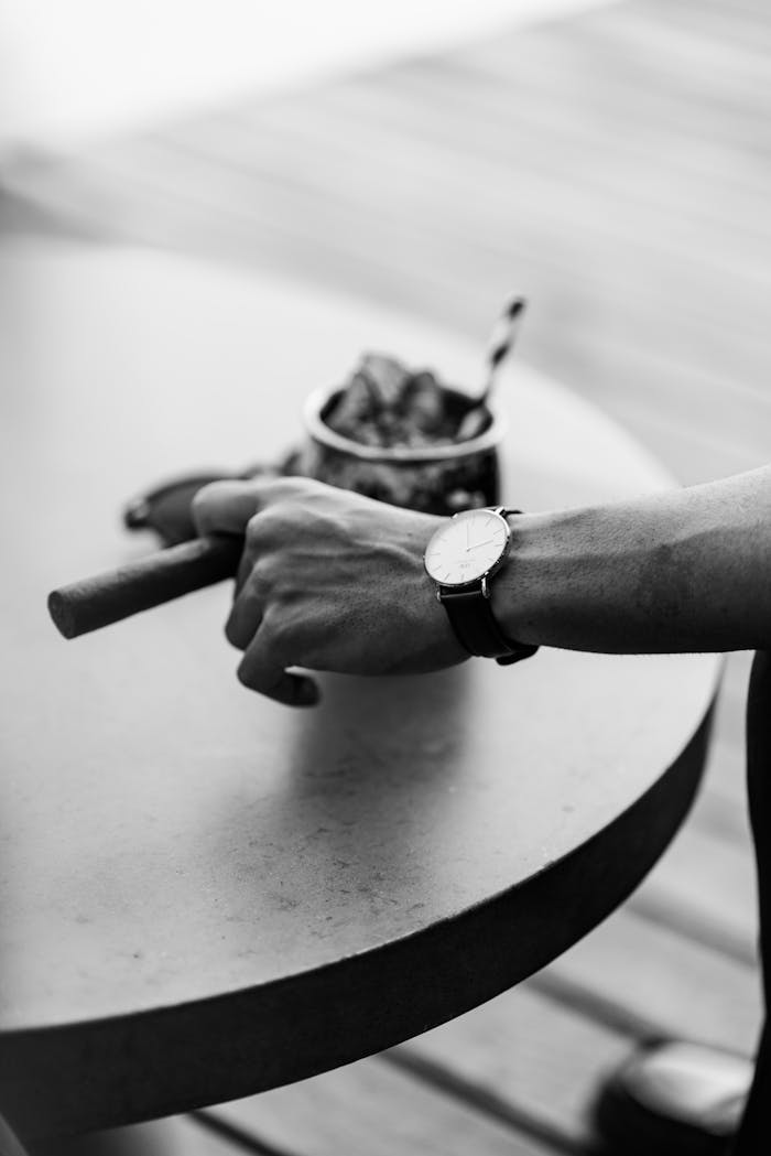 Home Stylish wristwatch and cigar on a table, captured in classic black and white.